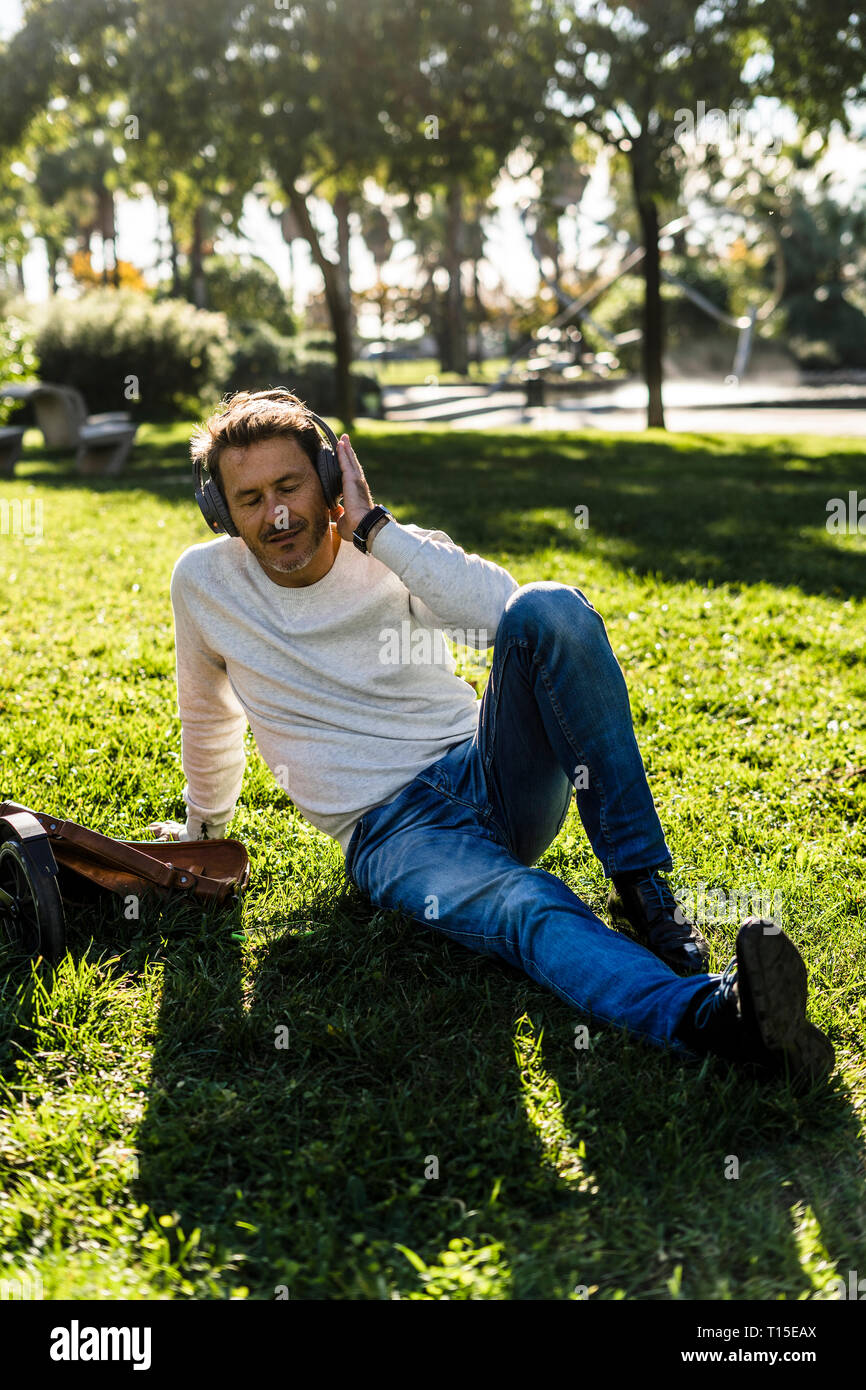 Imprenditore Casual prendendo una pausa in un prak, seduti su erba, ascolto di musica Foto Stock