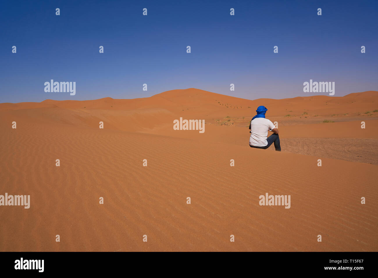 Il Marocco, vista posteriore di uomo seduto sulle dune del deserto Foto Stock