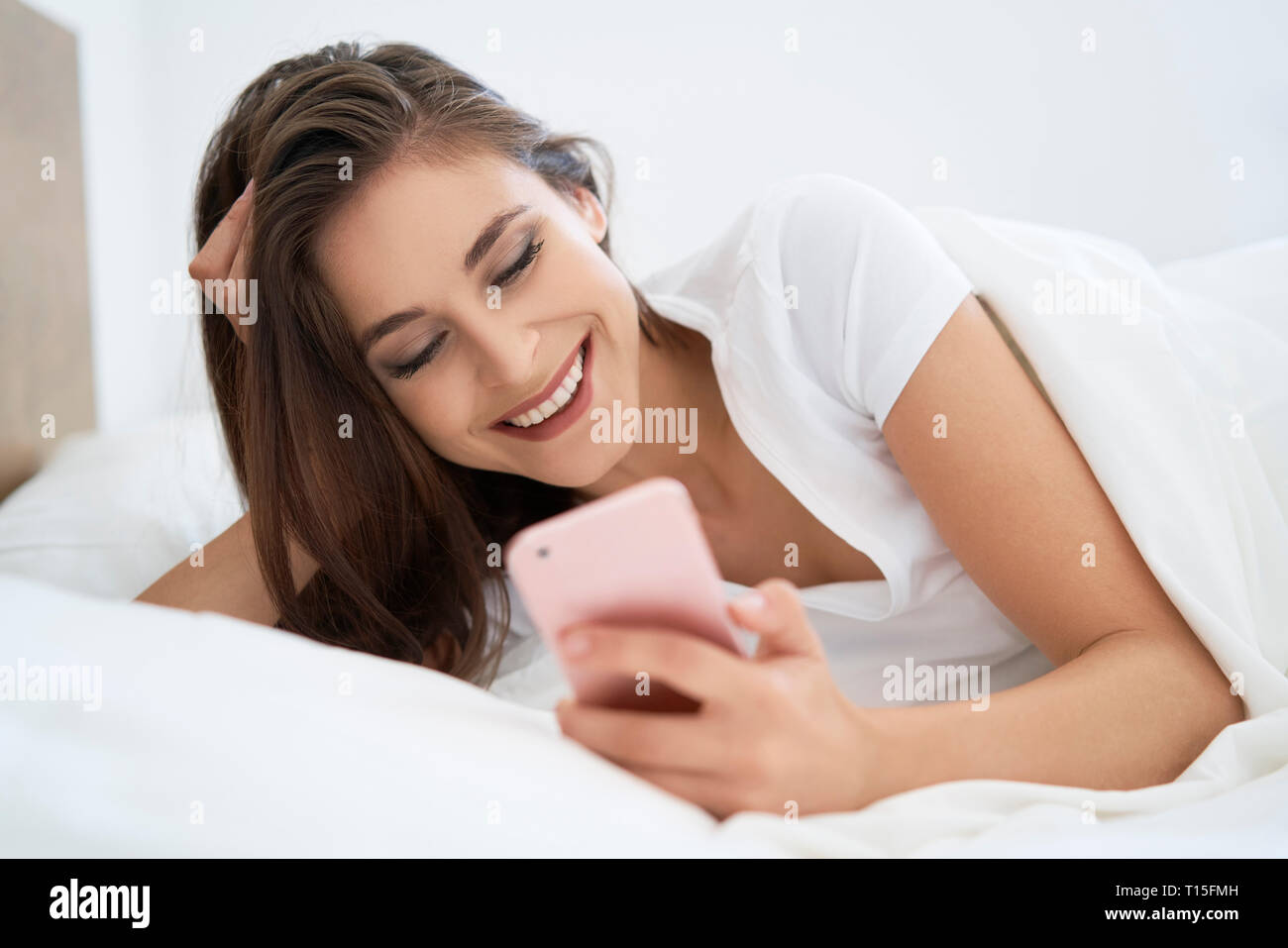 Giovane donna giaceva sul letto, utilizza lo smartphone Foto Stock