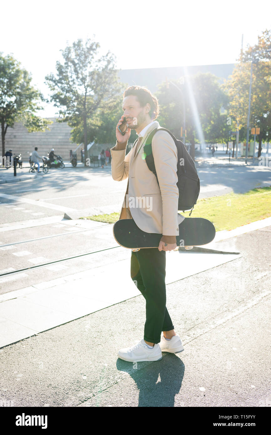 Uomo al telefono con zaino e skateboard in città Foto Stock