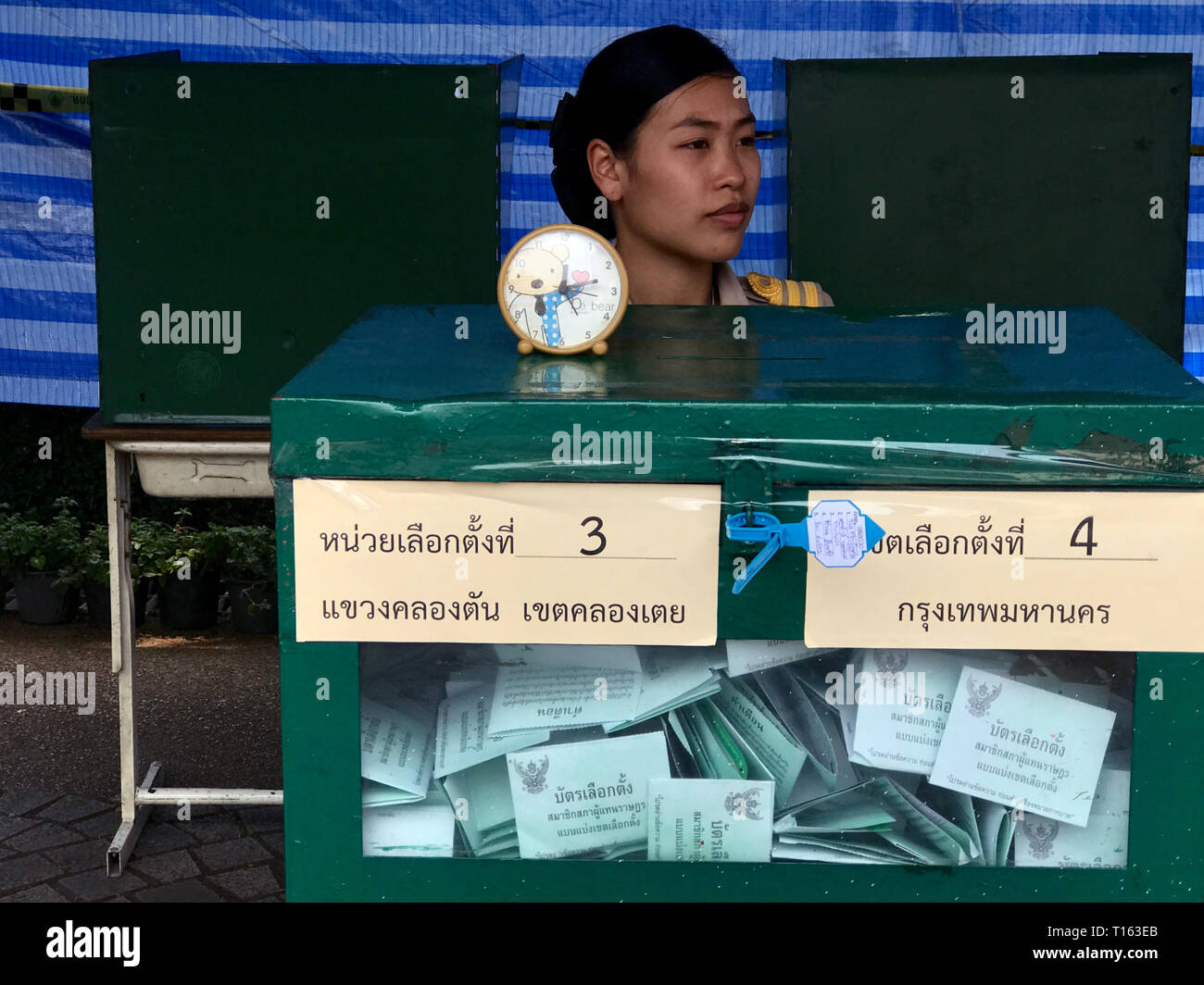 Bangkok, Tailandia. 24 Mar, 2019. Elezione di un lavoratore è seduta in una stazione di polling dietro un'urna. Quasi cinque anni dopo un colpo di stato militare, elezioni parlamentari hanno iniziato in Thailandia. Credito: Christoph Sator/dpa/Alamy Live News Foto Stock