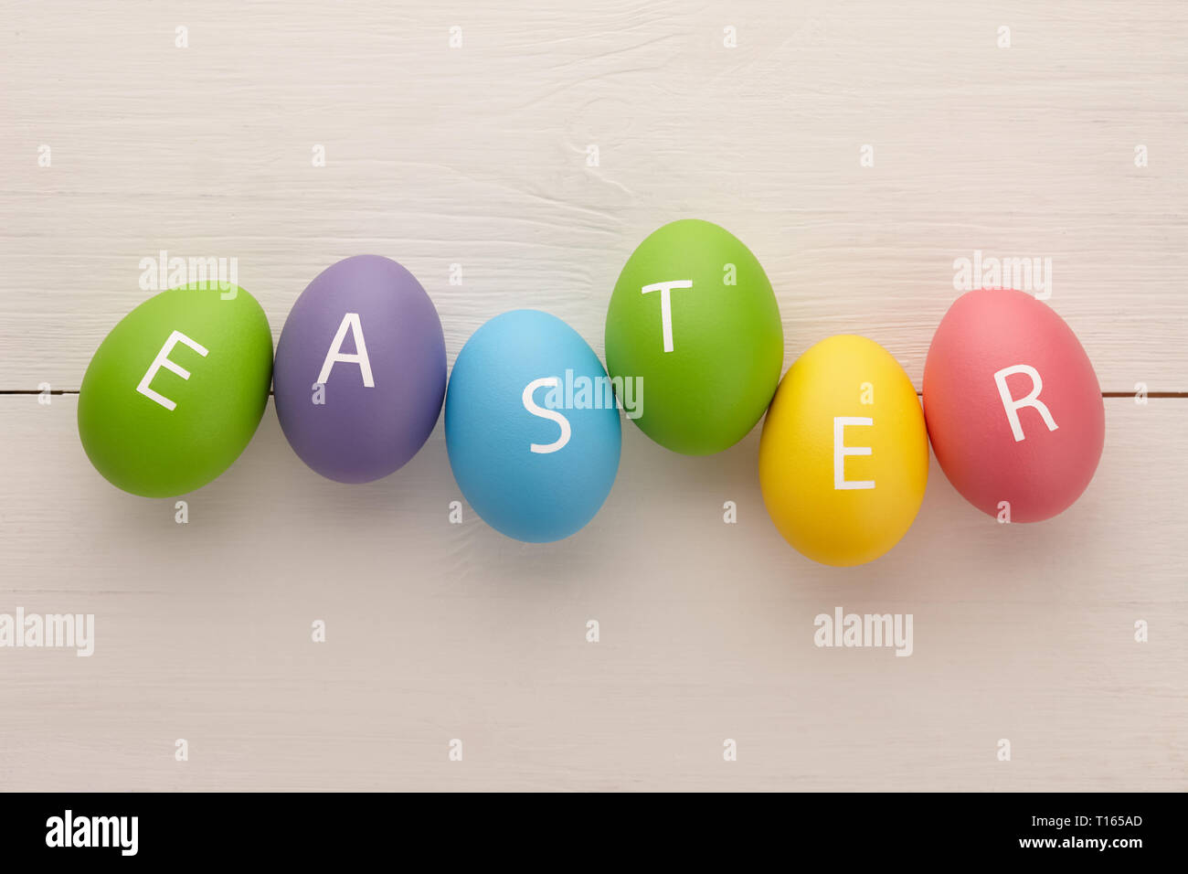 Verniciato colorato uova con lettere disposte in una parola la Pasqua su bianco tavole di legno dello sfondo. Concetto di vacanza. Foto Stock