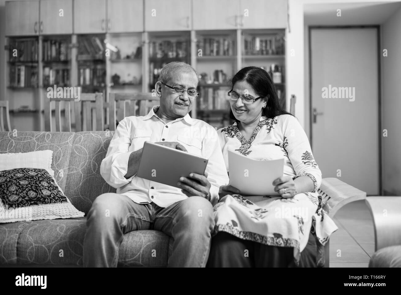 Contabilità di coppia indiana/asiatica senior, facendo finanza domestica e controllando le fatture con il laptop, la calcolatrice e i soldi mentre si siede sul divano/divano a casa Foto Stock