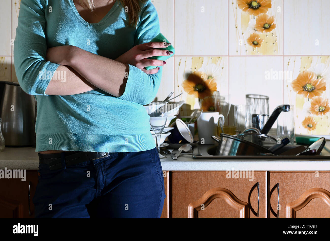 Frammento del corpo femminile presso il bancone cucina, riempito con un sacco di piatti non lavati. La ragazza è stanco di affrontare il compito quotidiano di lavaggio d Foto Stock