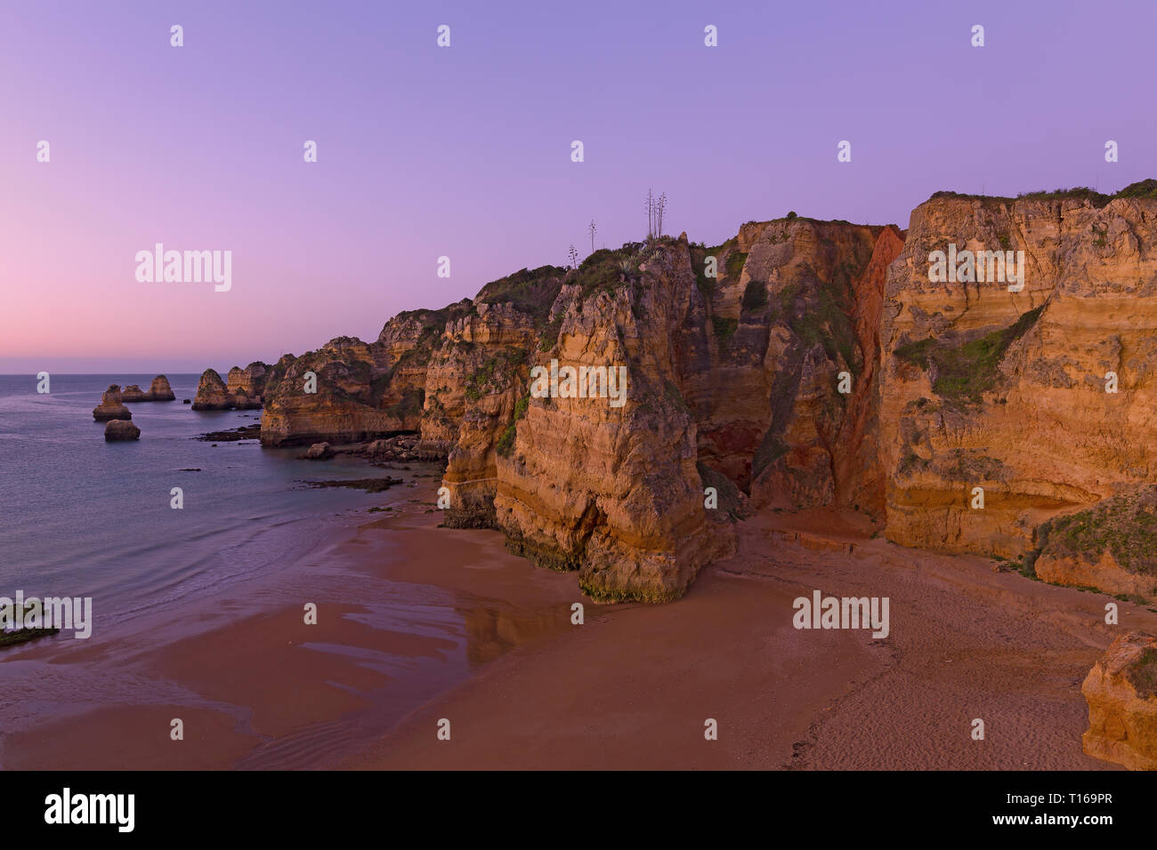 Vuoto spiaggia sabbiosa con un tocco di stravaganza scogliere a sunrise di Lagos, Portogallo. Nuvoloso Tramonto sull'Oceano Atlantico. Foto Stock