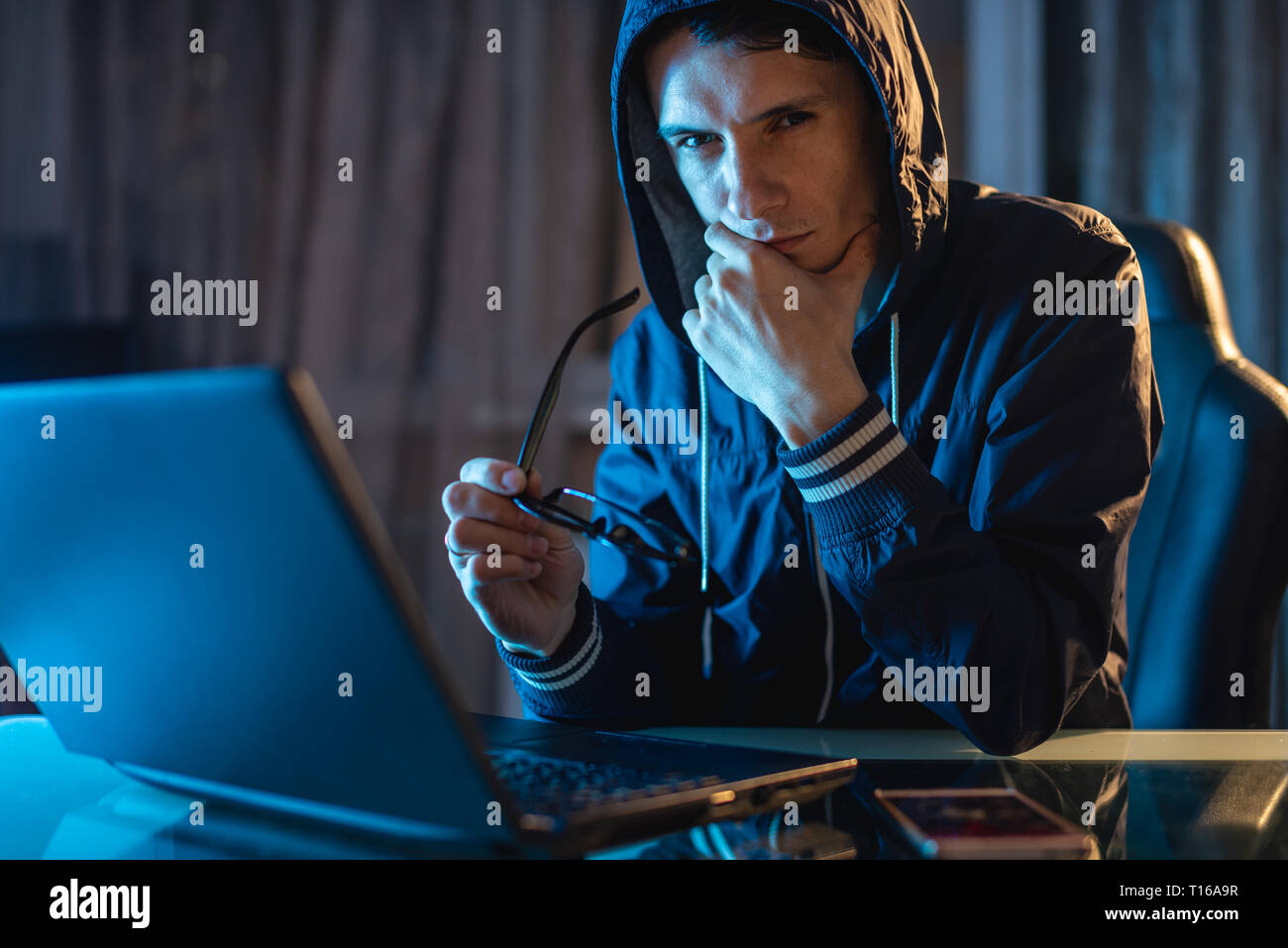 Maschio nel cofano cercando nella fotocamera. Attacchi di hacker e il furto di accedere ai database con password. Il concetto di sicurezza informatica Foto Stock