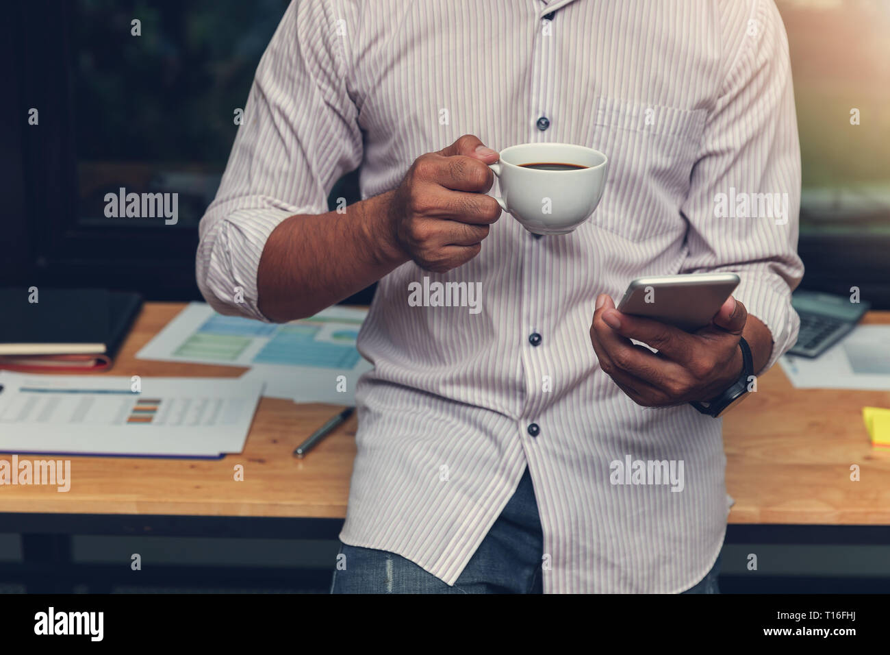 Affari e finanza concetto di ufficio a lavorare, imprenditore utilizza lo smartphone e azienda tazza da caffè in ufficio Foto Stock