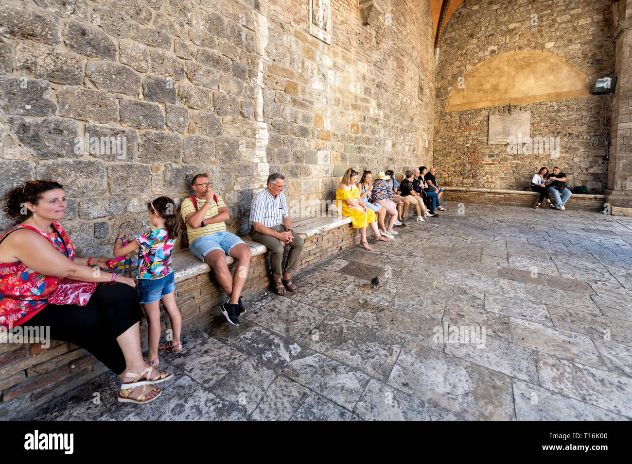 San Gimignano, Italia - 27 agosto 2018: Molte persone sedute in appoggio sulle panchine in piccola e antica città medievale Borgo in Toscana durante il giorno di estate Foto Stock