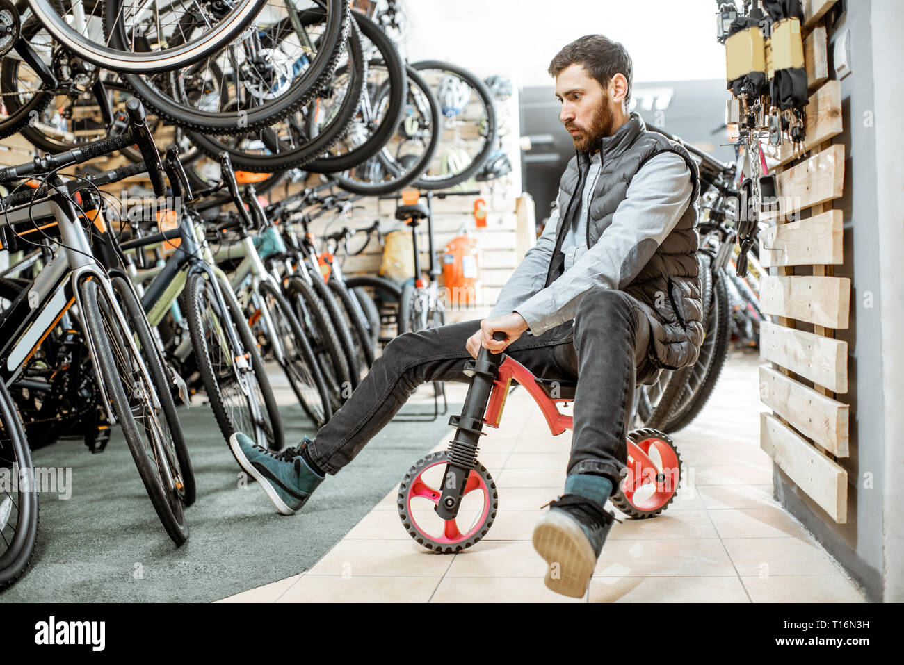 Divertente ritratto di un uomo a cavallo per bambini in bicicletta il negozio di biciclette e attrezzature sportive Foto Stock