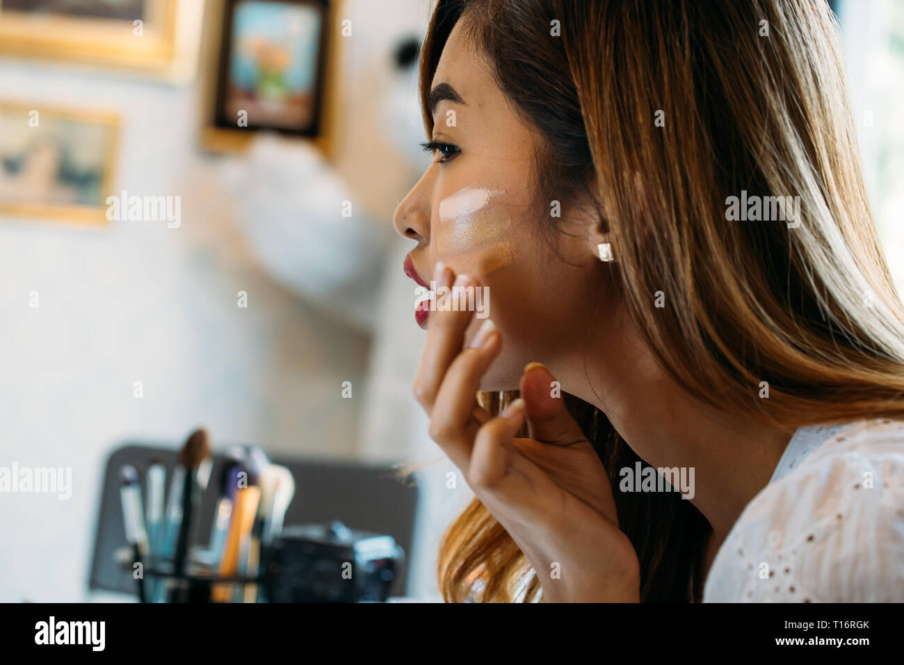 Closeup giovane donna asiatica con labbra rosse correttore di applicazione sulla faccia su sfondo sfocato Foto Stock