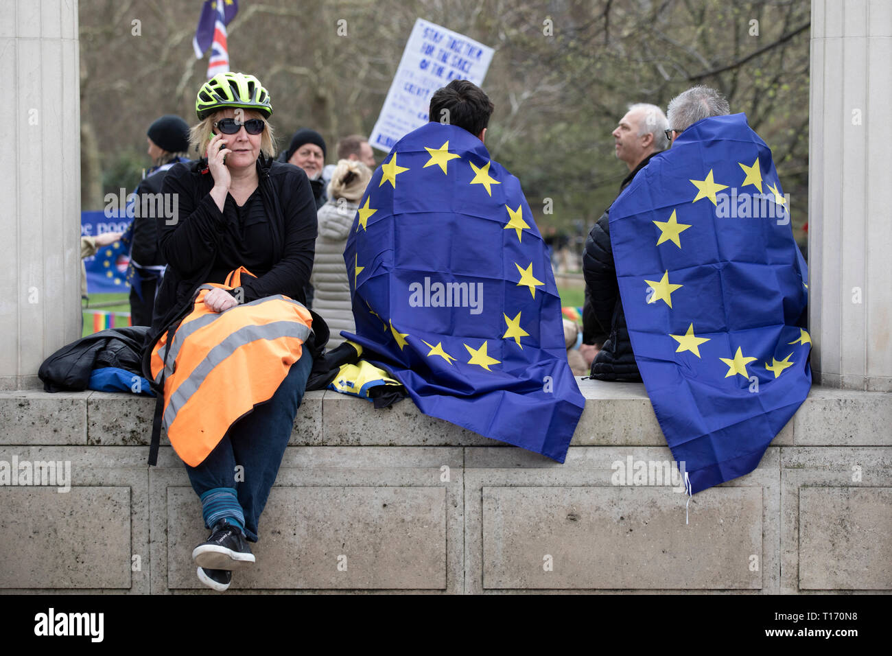 Donna al telefono e due persone avvolto in Unione Europea bandiere sat sul muro, voto popolare marzo a Londra, Inghilterra Foto Stock