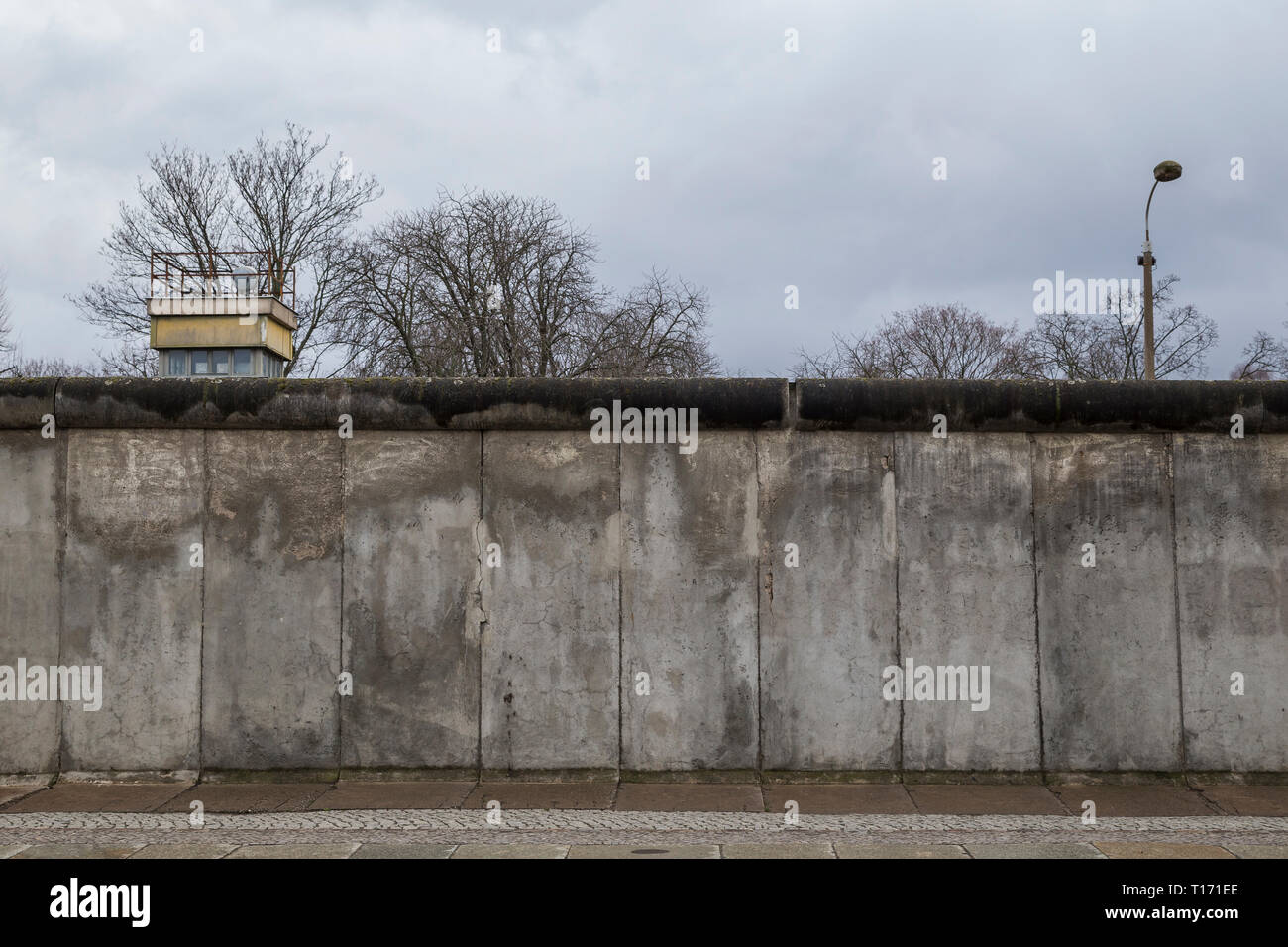 Vista frontale di una sezione originale del muro di Berlino e la torre di avvistamento al Memoriale del Muro di Berlino (Berliner Mauer) di Berlino, Germania, in un giorno nuvoloso. Foto Stock