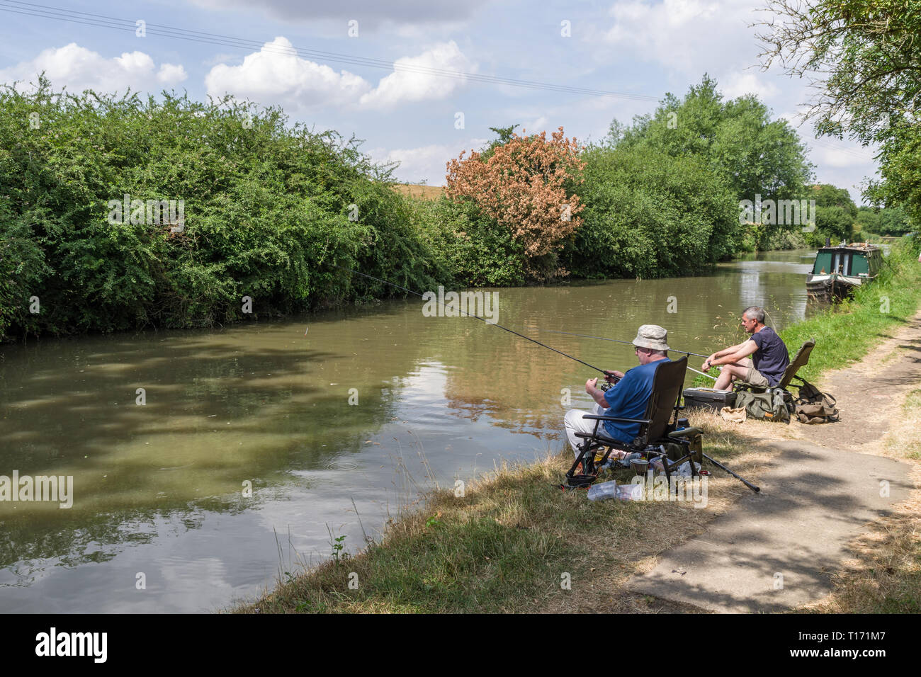 Due amici maschi, seduti fianco a fianco, pesca sul Grand Union Canal, Blisworth, Northamptonshire, Regno Unito Foto Stock