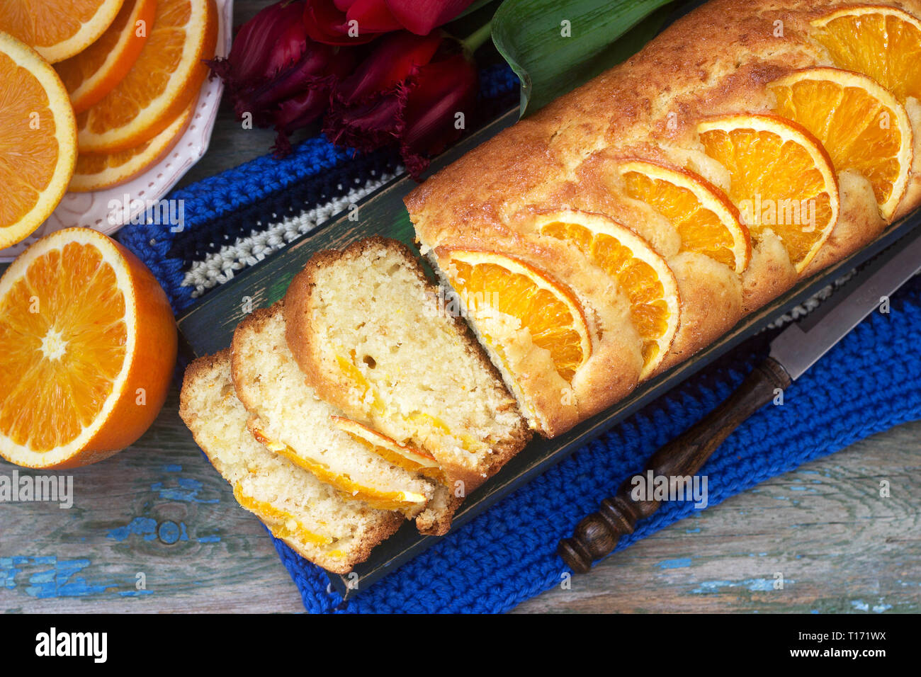 Arancio dolce, decorate con fette di arancia su uno sfondo di succose arance e un mazzo di tulipani. Stile rustico. Foto Stock