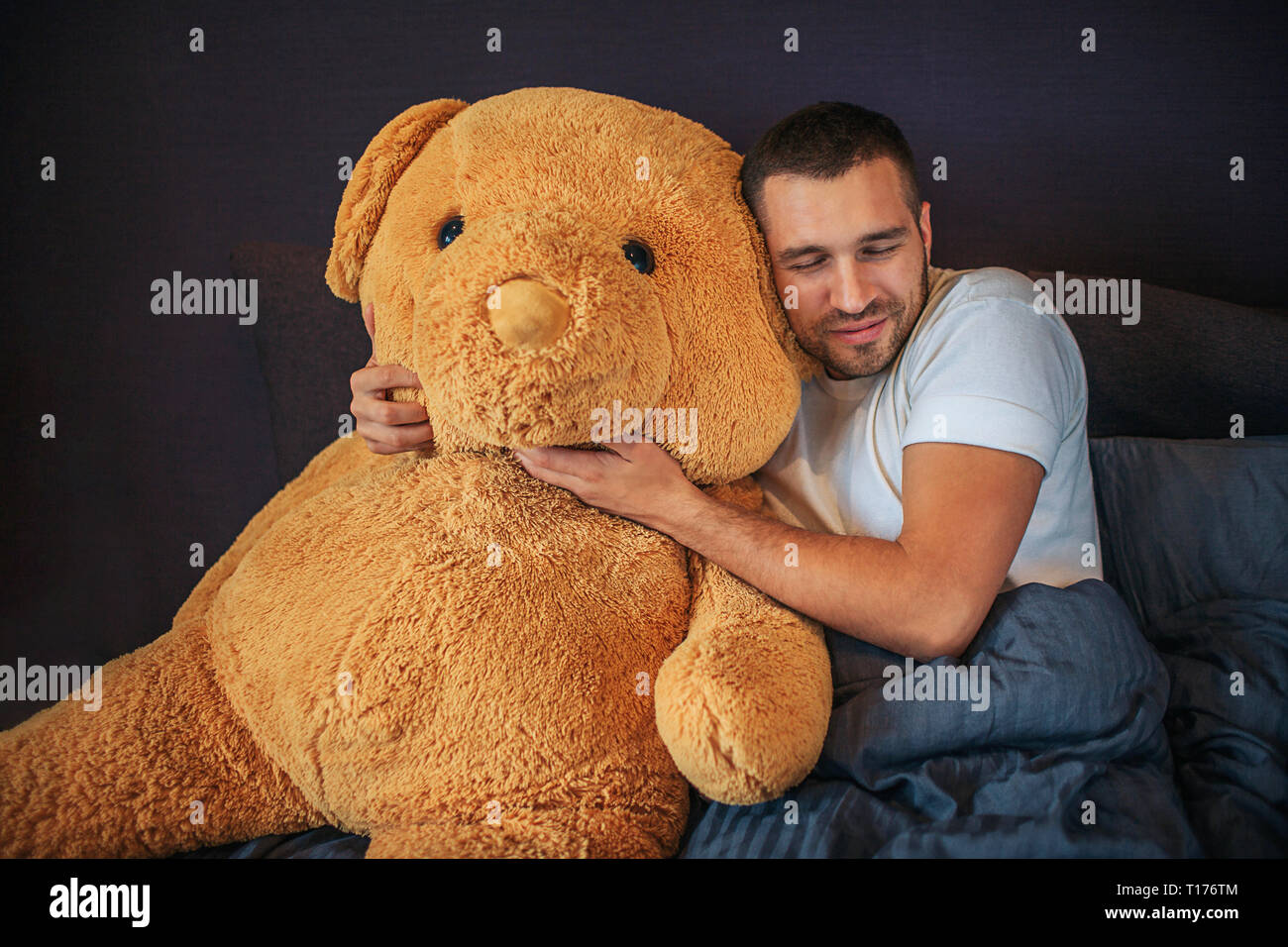 Bella immagine di adulto con grande orso arancione giocattolo. Guy abbracciare e si appoggia su di esso. Egli tiene gli occhi chiusi. L uomo ha il resto. È malato. Foto Stock