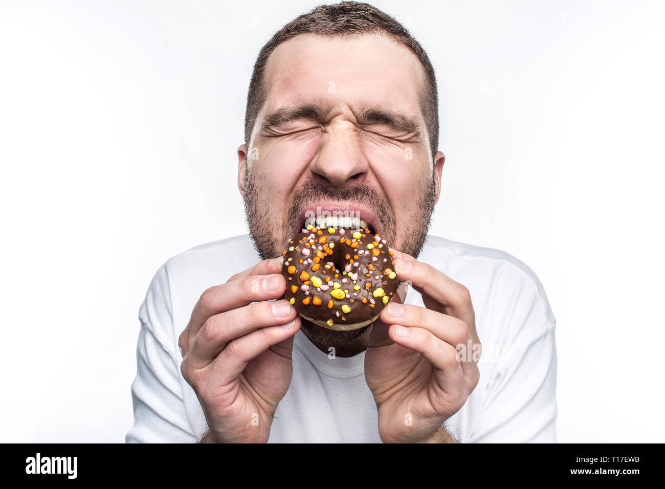 Questo ragazzo sta morendo di fame in modo egli è mangiare un Big fat ciambella di cioccolato. Egli ha chiuso gli occhi e godendo il momento. Ypoung uomo piace mangiare diversi tipi Foto Stock