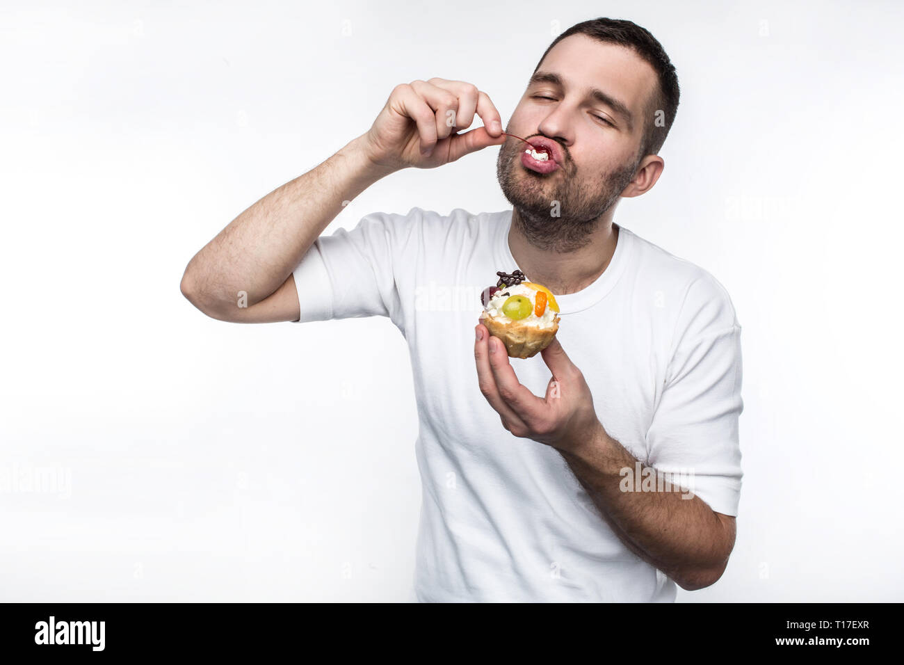 Adulto è divouring dolce cremoso dessert. Egli sta godendo il processo di mangiarlo. Isolato su sfondo bianco. Foto Stock