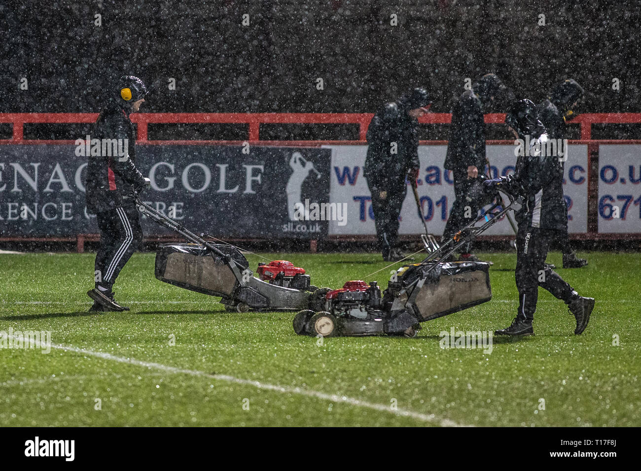 Il personale di terra e di taglio mantenendo erba sul campo di calcio in heavy rain Foto Stock