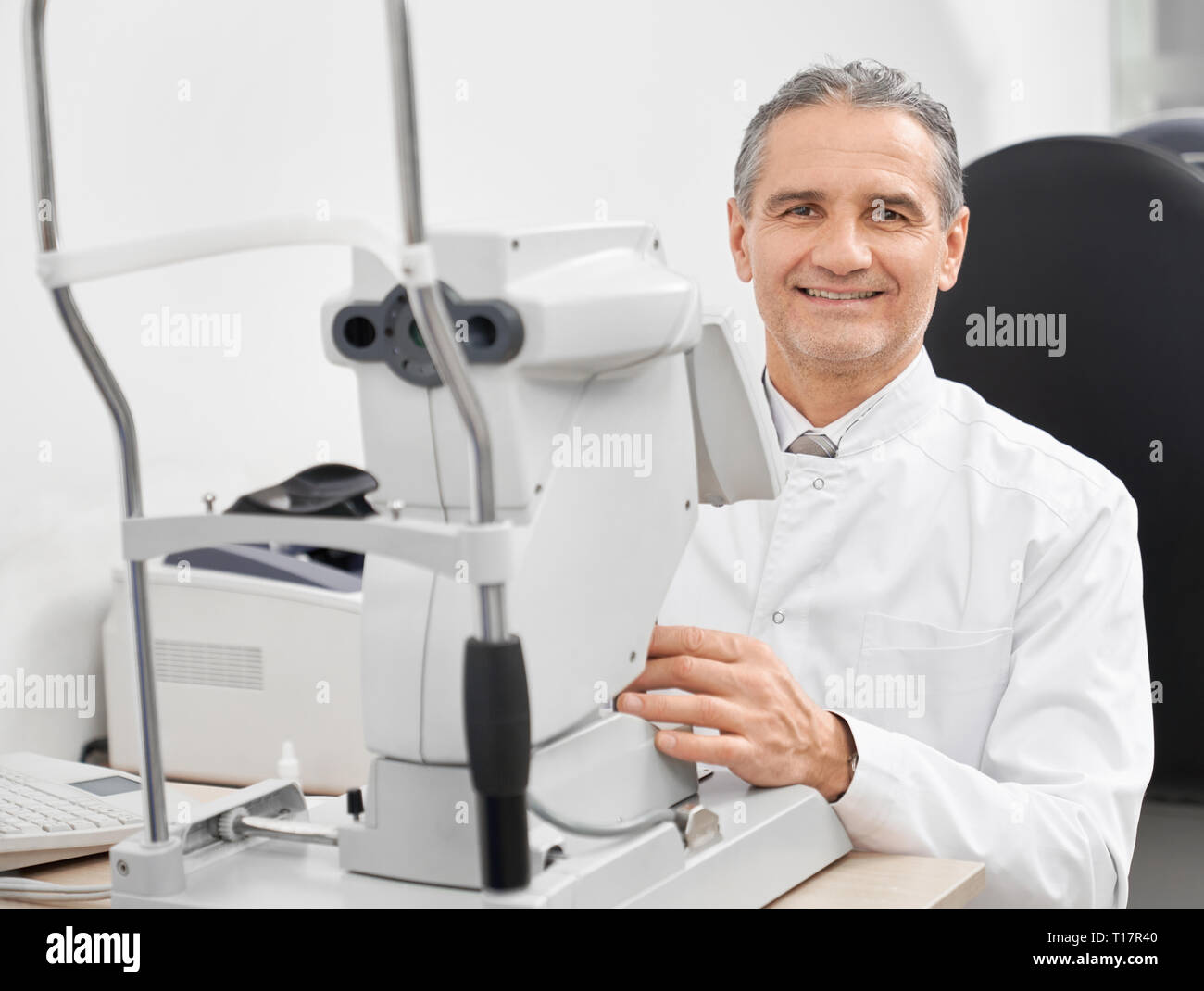 Medico esperto oculista posa con lampada a fessura, occhio macchina da test. Sorridere all'ottico optometrista seduta a tavola con apparecchiature speciali per la verifica visiva delle clinica moderna. Foto Stock