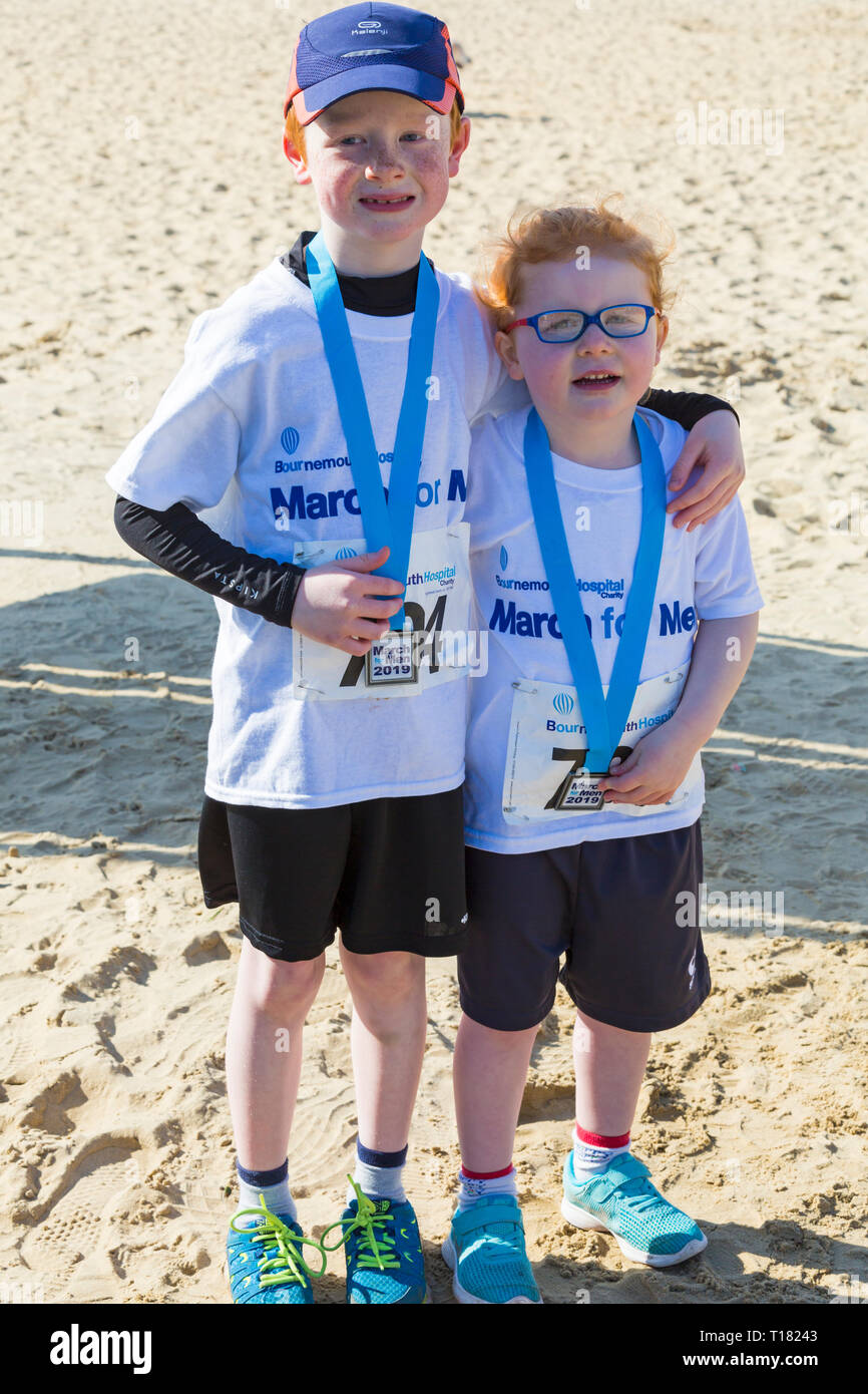 Bournemouth, UK. 24th Mar 2019. March for Men - men of all generations, sons, fathers, brothers, uncles, grandfathers, as well as women, girls and dogs, gather in Bournemouth on a lovely warm sunny day to walk, jog or run 1km, 5km or 10km, organised by Bournemouth Hospital Charity. It highlights health concerns men face such as prostate or testicular cancer. The fundraising event helps raise funds to support treatment and new equipment to improve care. Holly and Sam with their medals. Credit: Carolyn Jenkins/Alamy Live News Foto Stock
