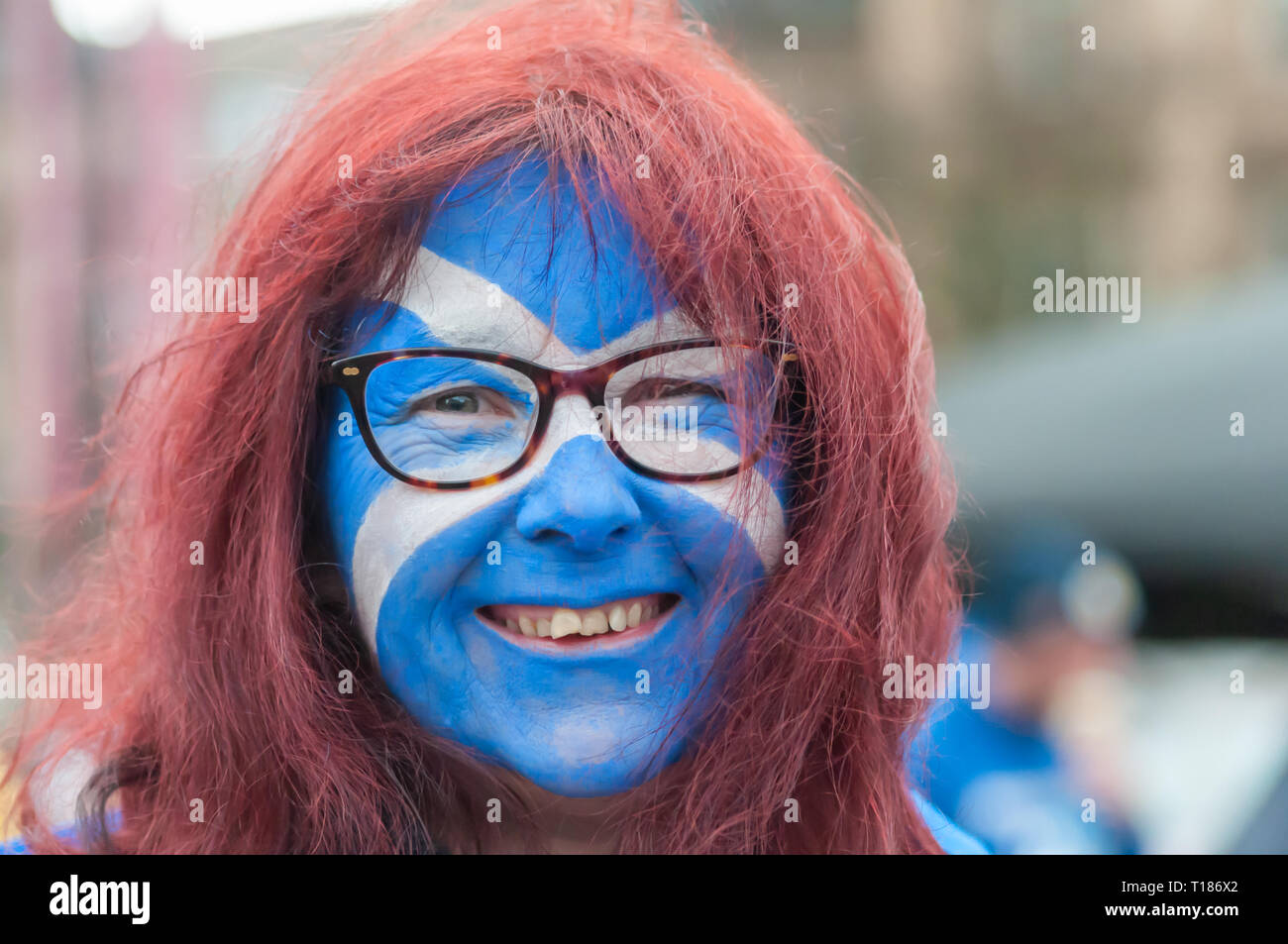 Glasgow, Scotland, Regno Unito. Il 24 marzo 2019. Donna sorridente con i capelli rossi, indossare occhiali e la bandiera della Scozia dipinta sul suo viso si unisce gli attivisti a sostegno dell indipendenza scozzese come si raduna per un rally a George Square.Il rally è stato organizzato dal gruppo di speranza sulla paura. Credito: Berretto Alamy/Live News Foto Stock