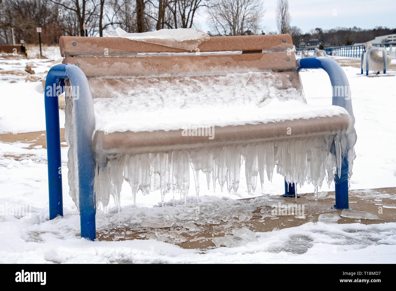 Ghiaccioli appesi su blu vacante una panchina nel parco in inverno Foto Stock