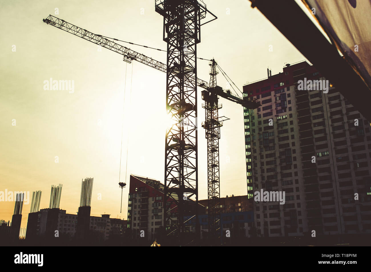 Sito di costruzione con alto edificio in costruzione in un ambiente urbano dominato da una grande gru industriali stagliano contro il cielo al tramonto Foto Stock