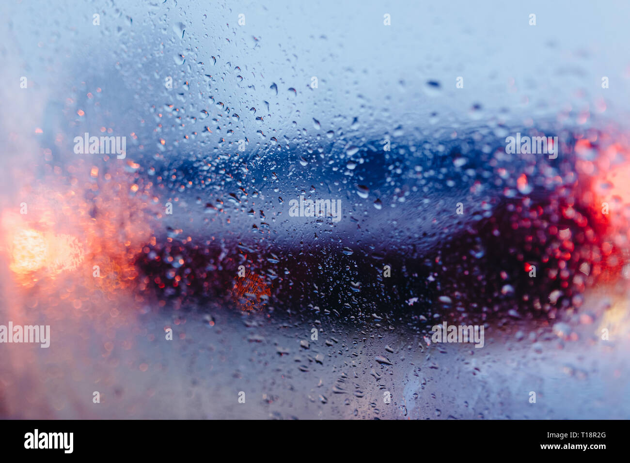 La città di notte la strada attraverso il parabrezza auto sfondo astratto goccia d'acqua sul vetro luci e pioggia Foto Stock