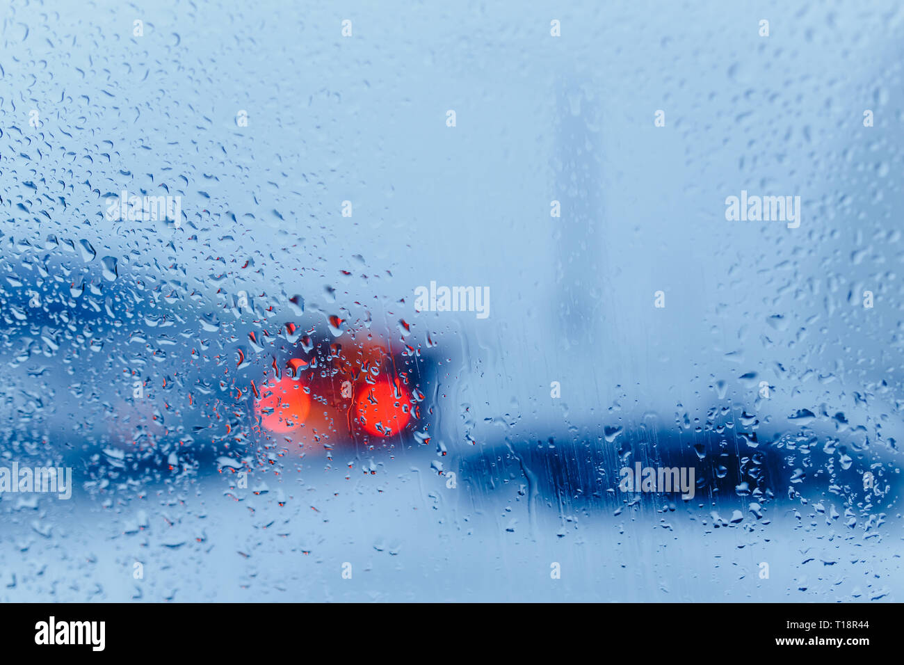 Abstract del traffico in caso di pioggia. Visto il traffico all'interno dell'auto. Gocce di pioggia sul parabrezza di auto e le luci di coda in bokeh di fondo Foto Stock