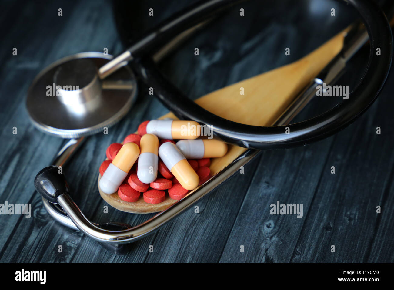 Pillole e capsule in un cucchiaio di legno e stetoscopio scuro su un tavolo di legno. Concetto di salute, farmaci, pressione sanguigna, vitamine, farmacia, trattamento Foto Stock