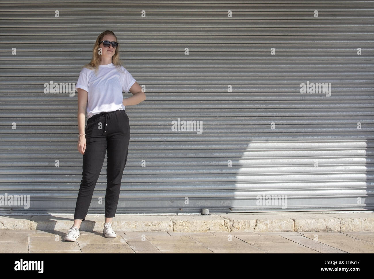 Foto completa del corpo del giovane sportivo casual vestito donna bionda con occhiali da sole in t-shirt bianco contro il ferro corrugato Wall street style Foto Stock