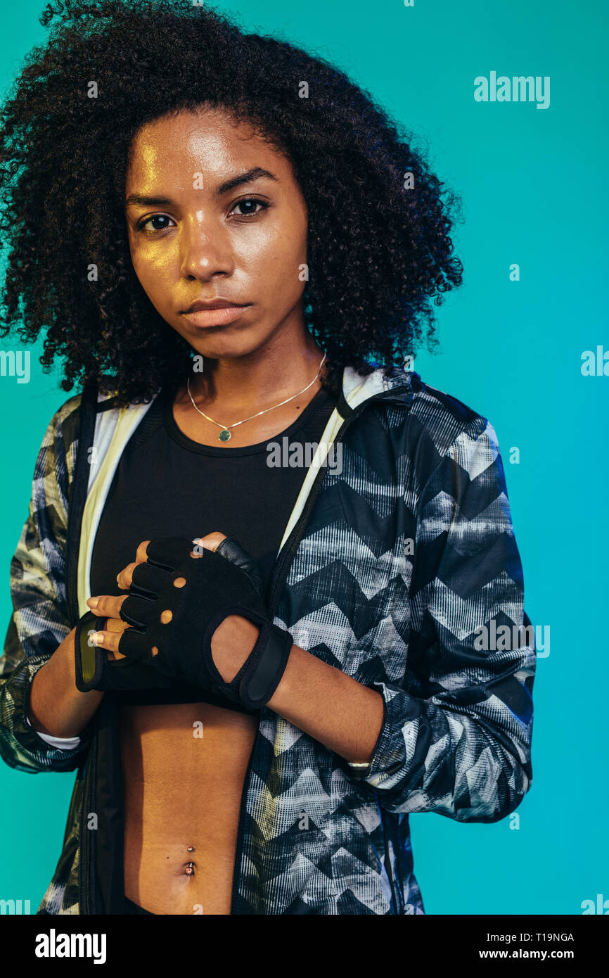 Robusto giovane donna in abbigliamento sportivo in piedi su sfondo blu. Montare femmina indossando i guanti pronto per l'allenamento in studio. Foto Stock