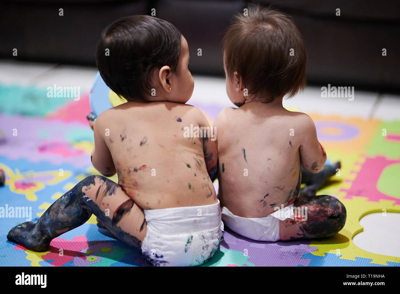 Bambini sporchi con vernice seduta di schiena sul pavimento Foto Stock