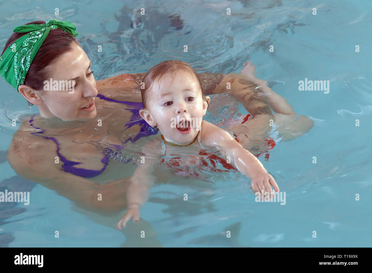 Madre giovane reale che impara con la sua figlia del toddler per nuotare alla piscina dove la fiducia e un legame è formato per la vita Foto Stock