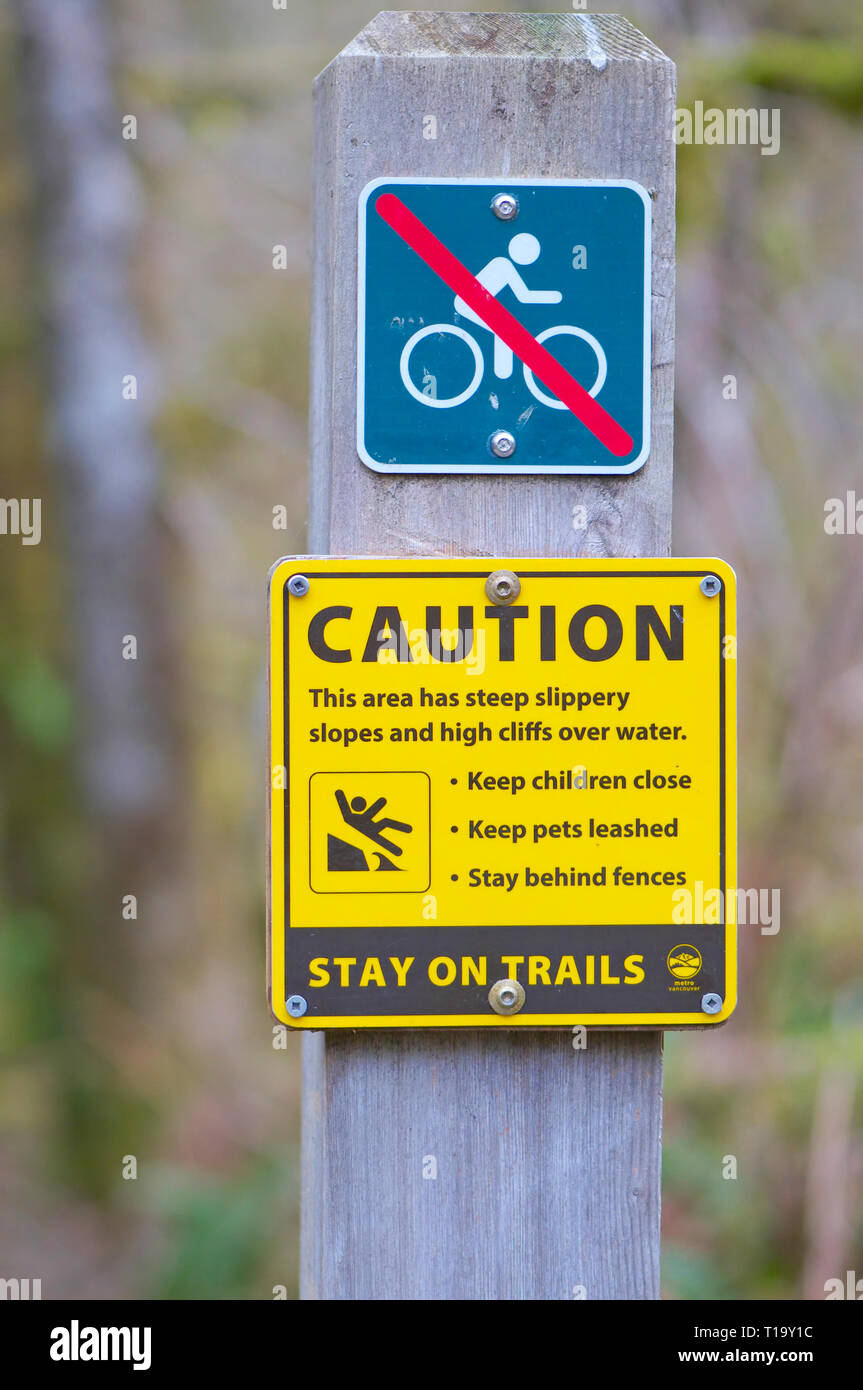 Giallo segno di attenzione e di un No bike segno avviso di persone a rimanere sui sentieri come la zona ha piste scivolose e alte scogliere sull'acqua. Foto Stock