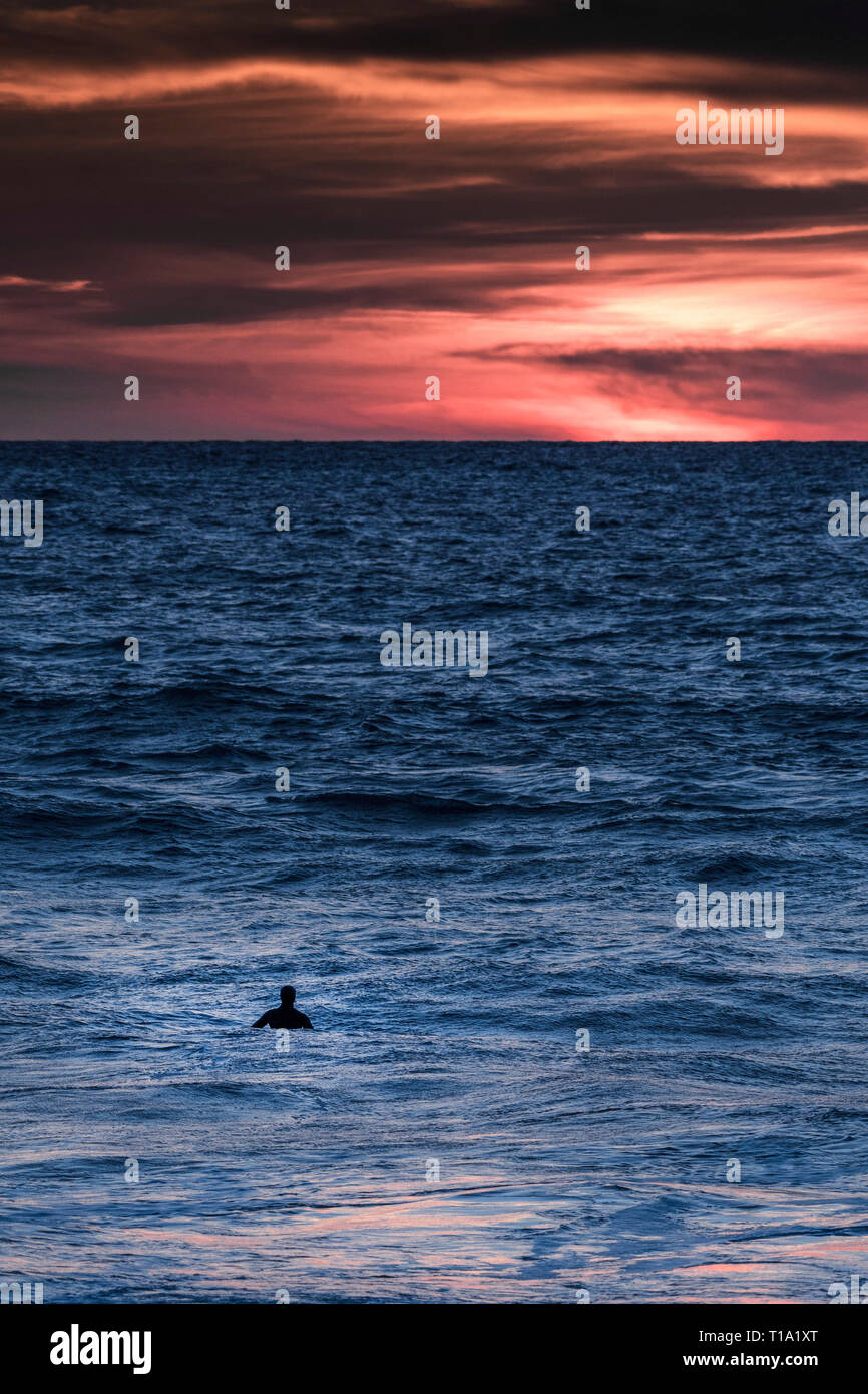 Un surfista in attesa di un'onda come il sole tramonta alle Fistral a Newquay in Cornovaglia. Foto Stock
