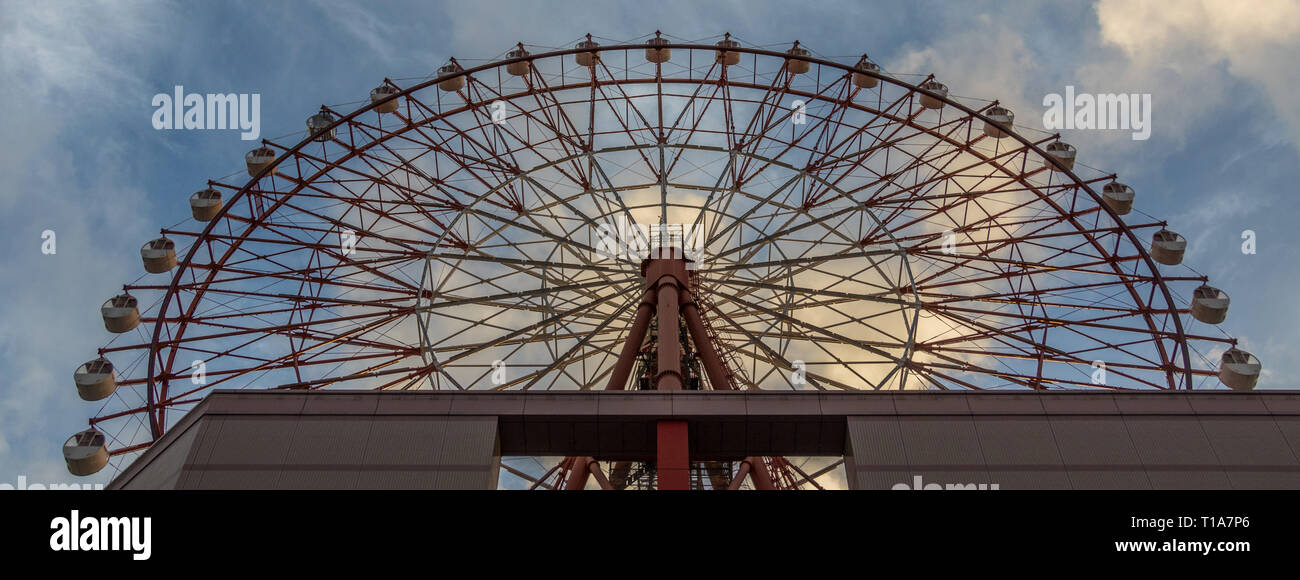 Red ruota panoramica Ferris di Amu Plaza a JR Kagoshima Chuo Station contro il cielo blu. Presa dal fondo. Situato a Kagoshima, Kyushu, a sud del Giappone. Foto Stock