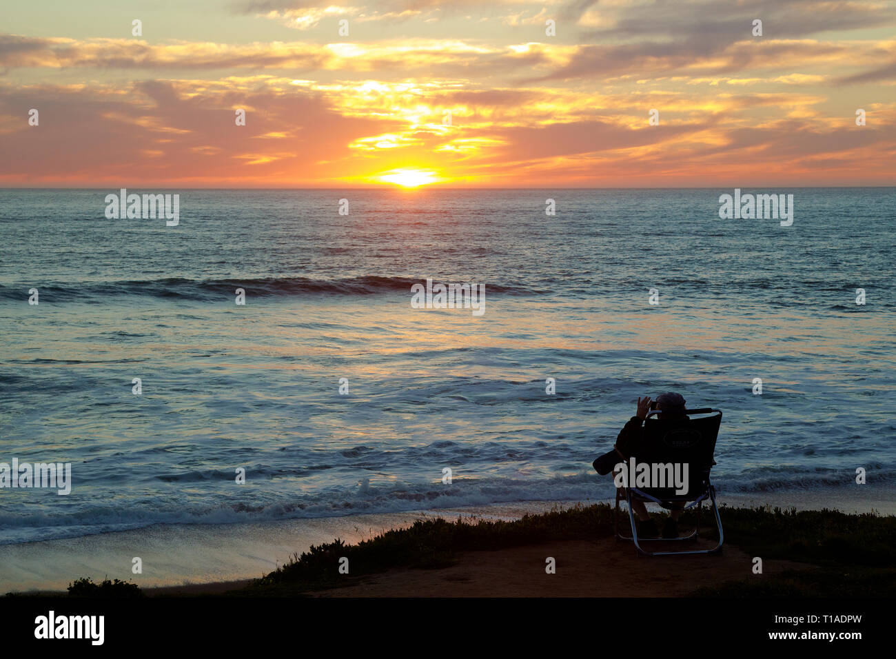 Persona seduta nel prato sdraio in Bluff guardando il tramonto sull'Oceano Pacifico Foto Stock