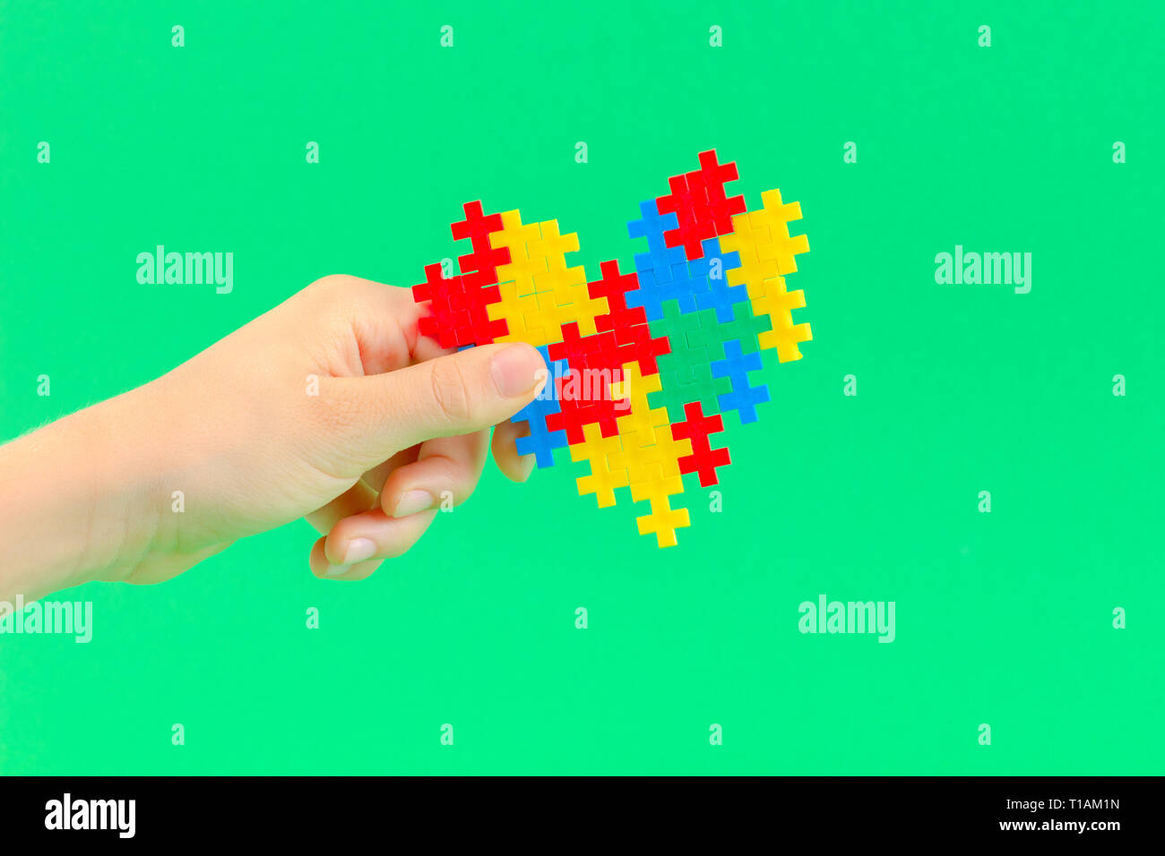 Bambino mano azienda cuore colorati su sfondo verde. Mondo autismo consapevolezza giorno di concetto Foto Stock