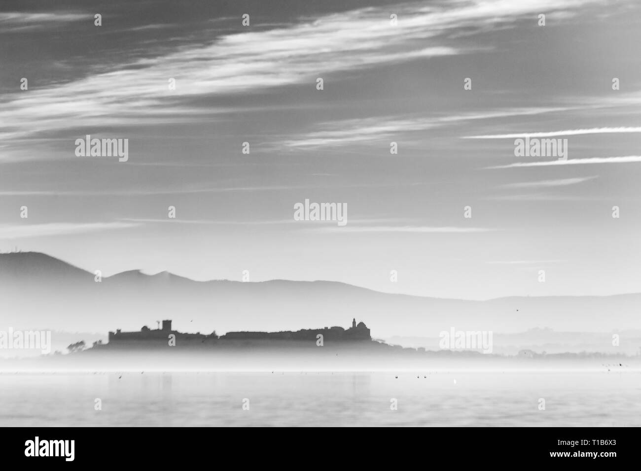 Bellissima vista del lago Trasimeno al tramonto con gli uccelli in acqua e di Castiglione del Lago Città Foto Stock