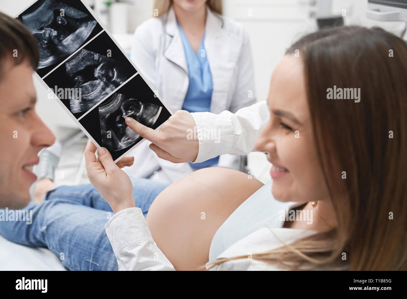 Donna incinta sorridente, azienda x ray, guardando il marito. Un futuro felice il Padre e la madre per la consultazione con il medico, facendo diagnostica ad ultrasuoni di addome in clinica medica. Foto Stock