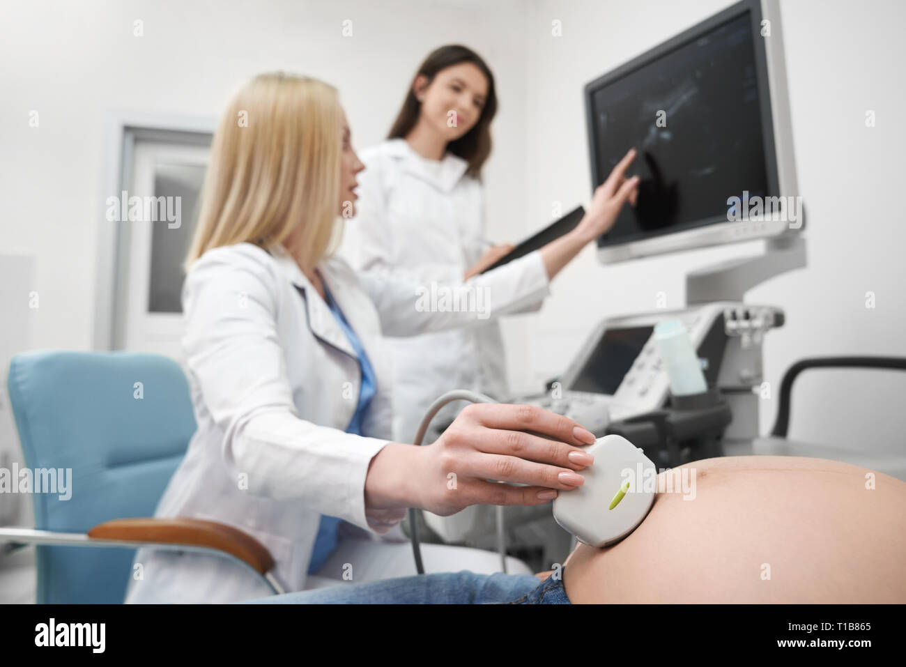 Medico professionale dispositivo di trattenimento, guardando il monitor della macchina ad ultrasuoni. Terapista esaminando l'addome della donna gravida. L'infermiera apposita cartella, lavorando in clinica medica. Foto Stock