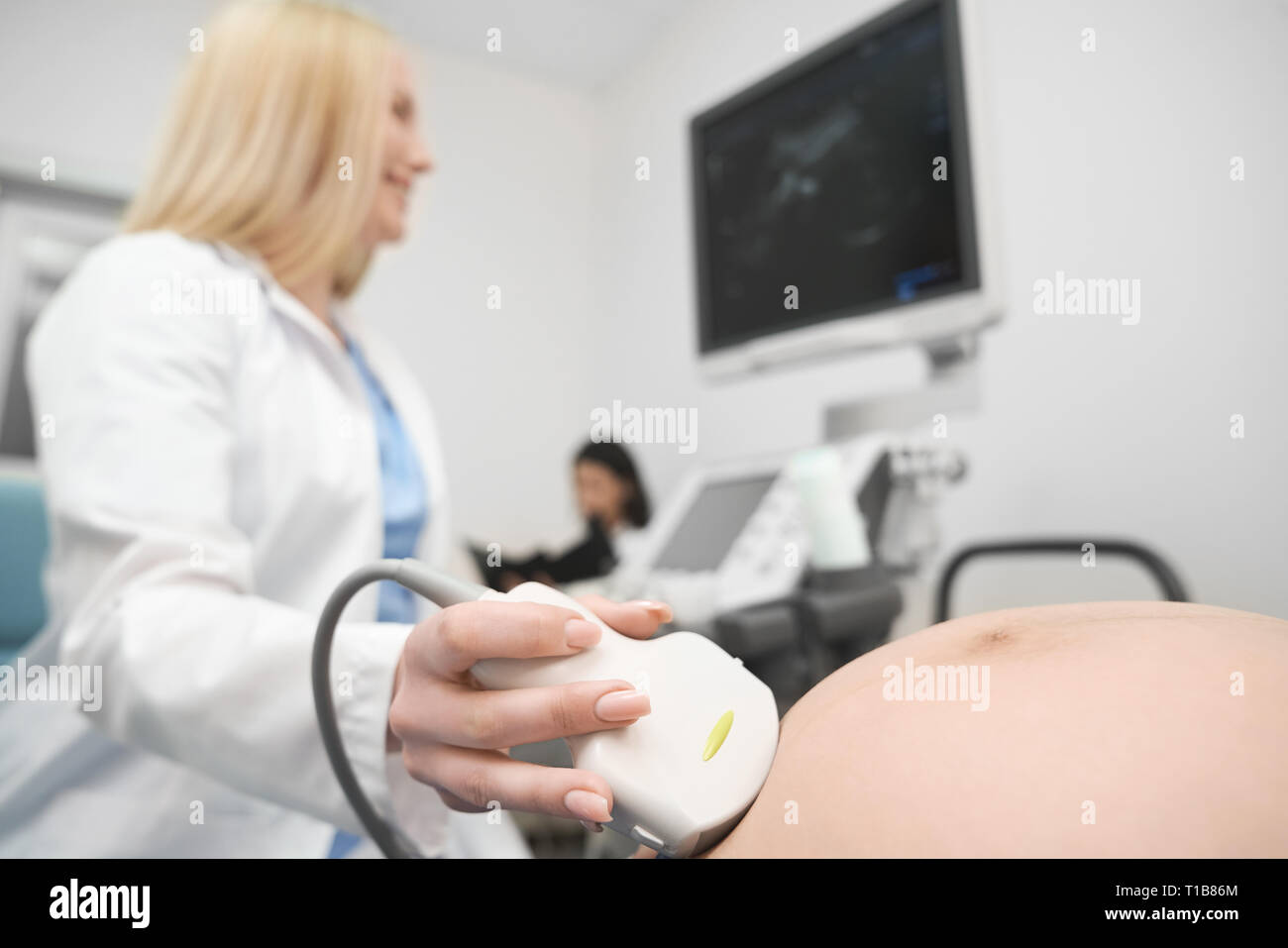 Close up di addome in stato di gravidanza della donna e medico di fare diagnosi ecografica. Terapeuta utilizzando il dispositivo, macchina ad ultrasuoni. Concetto di moderna clinica, medicina e gravidanza. Foto Stock