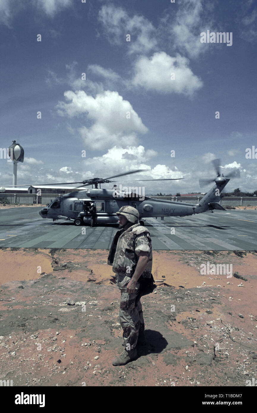 Il 29 ottobre 1993 A U.S. Soldato dell'esercito si erge in primo piano come un US Navy Sikorsky SH-60 Seahawk elicottero dall'USS Abraham Lincoln si prepara per il decollo dalla heli-pad a UNOSOM HQ a Mogadiscio, in Somalia. Foto Stock