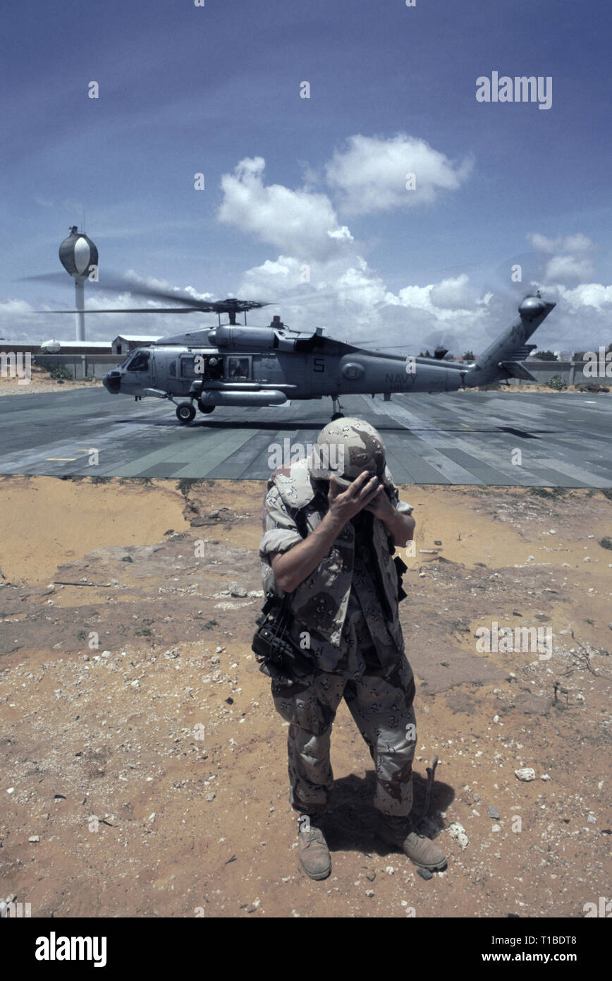 Il 29 ottobre 1993 A U.S. Soldato dell'esercito gira le spalle per la tempesta di sabbia come un US Navy Sikorsky SH-60 Seahawk elicottero dall'USS Abraham Lincoln decolla dall'heli-pad a UNOSOM HQ a Mogadiscio, in Somalia. Foto Stock