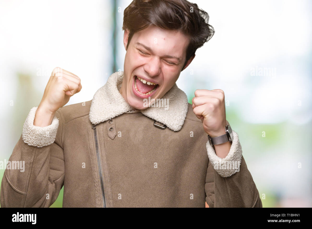 Giovane uomo bello indossare cappotto invernale su sfondo isolato molto felici ed eccitati facendo vincitore gesto con le braccia sollevate, sorridente e urlando fo Foto Stock