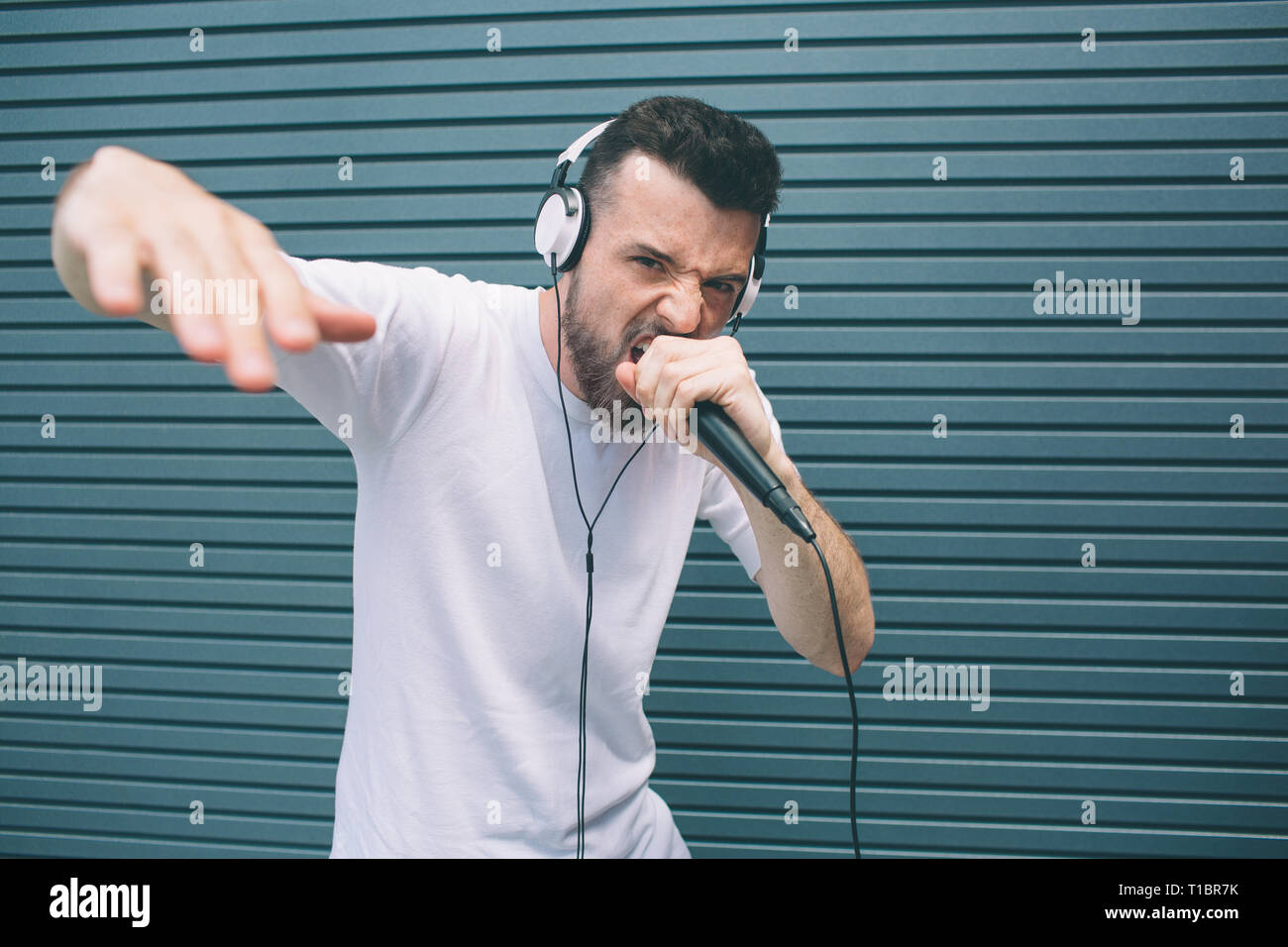 Cool e awesome l uomo è la lettura di rap nel microfono. È lui che mostra  la sua mano e guardando la fotocamera. Il ragazzo è cantare in mic e  indossa le
