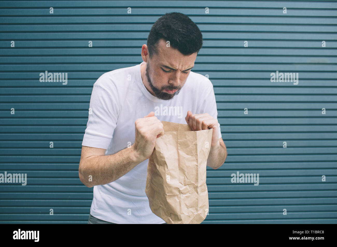 Una immagine di uomo malato cercando di vomito in sacchetto di carta. Egli si sente orribile. Isolato su striped e sfondo blu. Foto Stock