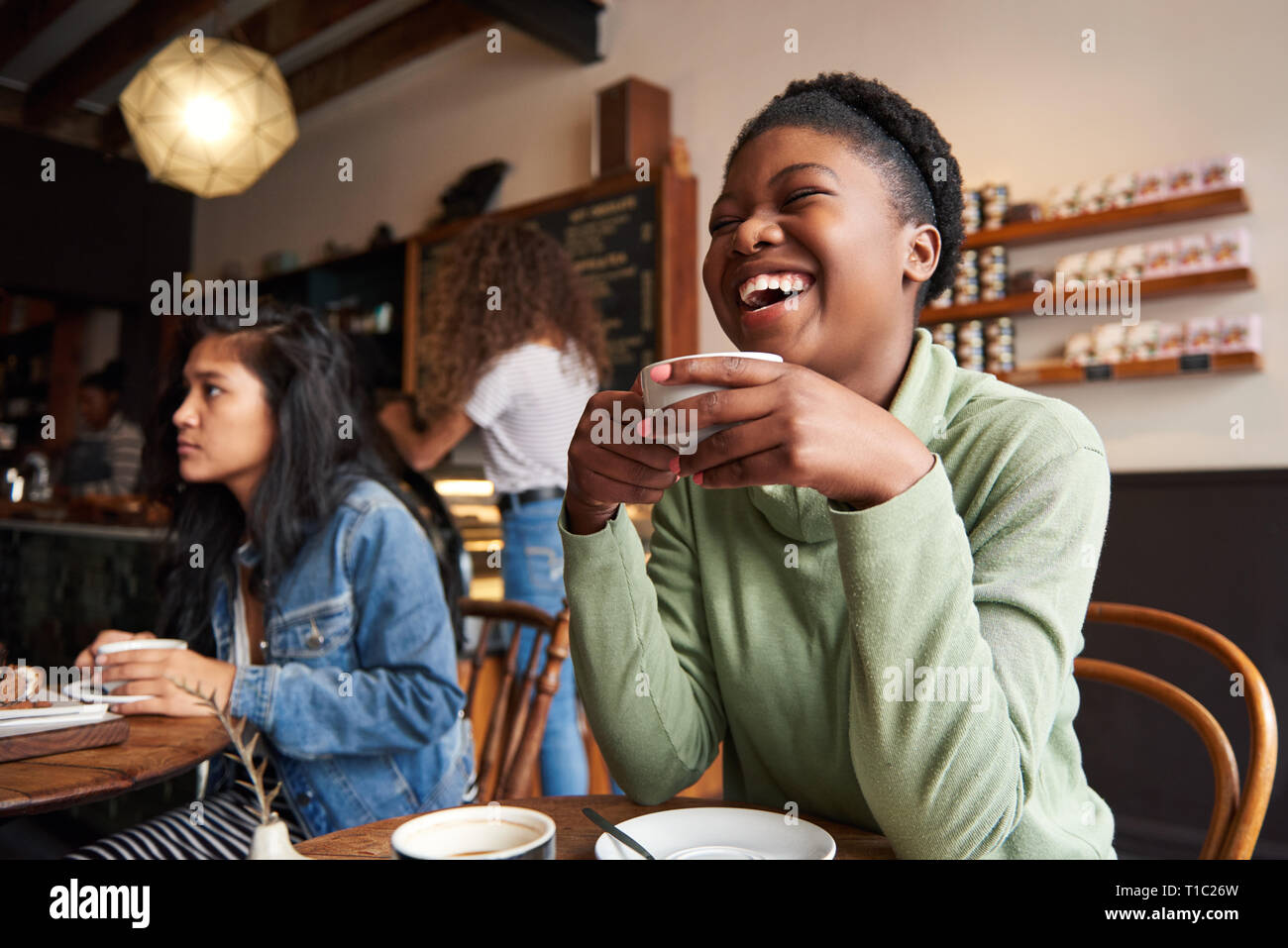Foto sincera di una giovane donna afroamericana che ride di un caffè con gli amici in un bar Foto Stock
