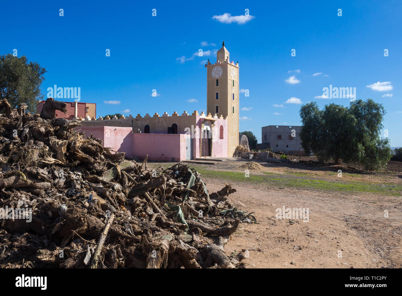 Pila di vari pezzi naturale del legno. Moschea con nuova facciata in background. Pentagramma marocchina sulla torre. Il cielo blu con nuvole bianche. Moroc Foto Stock